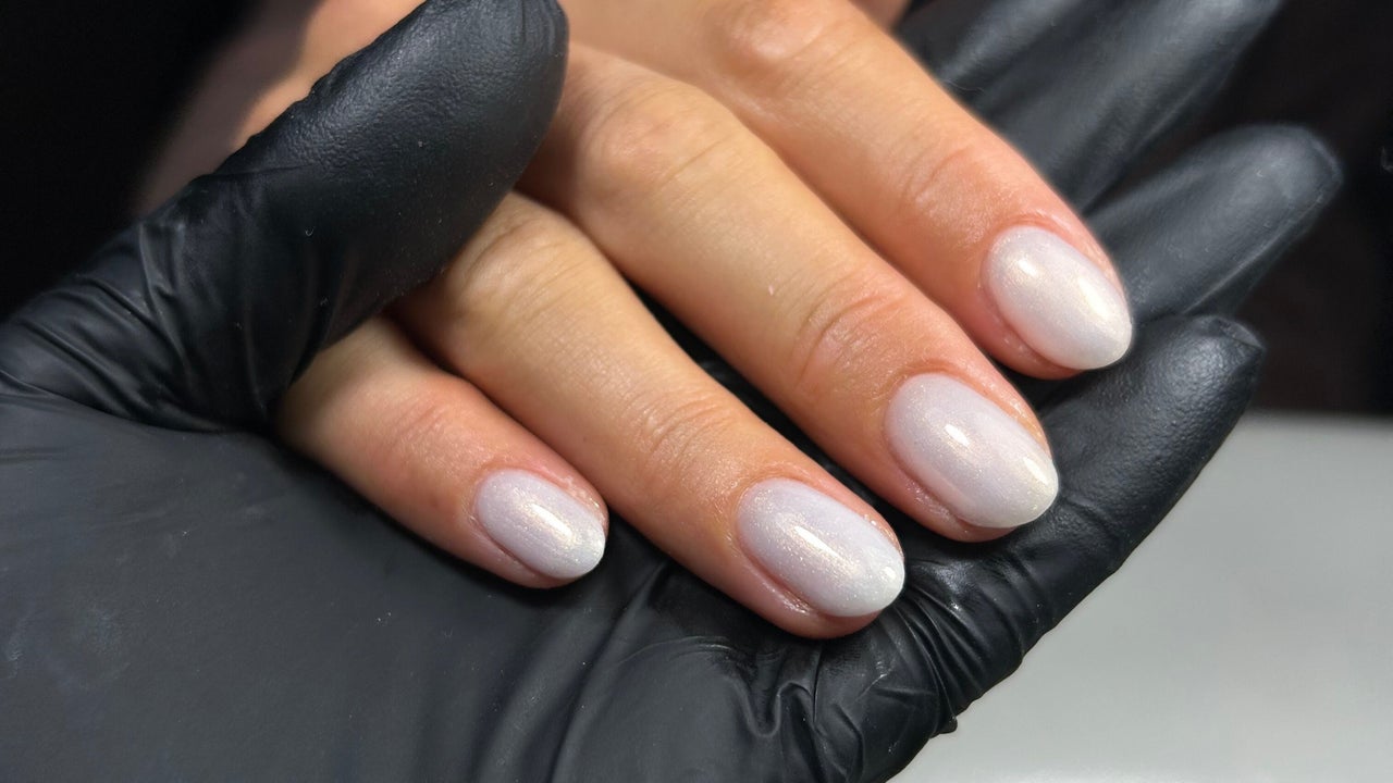 Melkwitte parelmoer amandelnagels op een zwarte handschoen